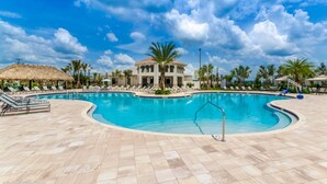 Ein Poolbereich eines Resorts mit großem Pool, Liegestühlen und Palmen.