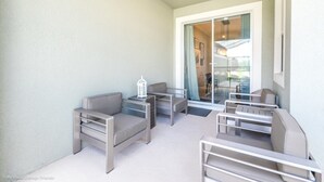 Ein Balkon mit zwei Sofas und einem kleinen Tisch, eine Glastür, die zu einem Außenbereich führt, und ein weißer Laternen auf dem Tisch.