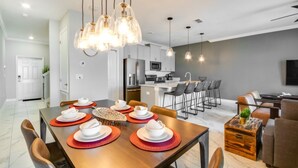 Eine moderne Küche mit Edelstahlgeräten, ein Essbereich mit einem Holztisch für vier Personen und ein Wohnbereich mit Sofa und Couchtisch.