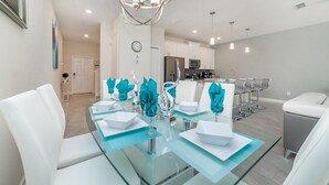 A modern dining area with a glass table, white chairs, and teal napkins. - Beautiful 5 Star Townhome on Storey Lake Resort With Private Pool, Orlando Townhome 4904 (Kissimmee)