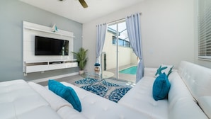 A modern living room with a white sofa, a glass coffee table, and a flat-screen TV mounted on a white wall. - Beautiful 5 Star Townhome on Storey Lake Resort With Private Pool, Orlando Townhome 4904 (Kissimmee)