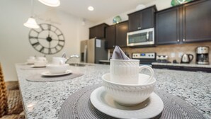 A kitchen with dark cabinets, a microwave, and a clock on the wall. - Beautiful Villa With First Class Amenities on Windsor at Westside Resort, Orlando Villa 4972 (Kissimmee)