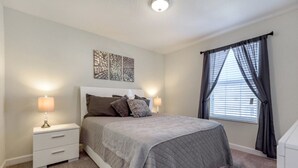Ein Schlafzimmer mit einem Bett, zwei Nachttischen mit Lampen, einem Fenster mit Vorhängen und einer Deckenleuchte.