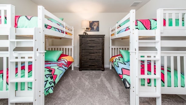 A room with bunk beds, a dark wooden cabinet, and a lamp on the wall. - The Ultimate Guide to Renting Your 5 Star Villa on Champions Gate Resort, Orlando Mansion 1817 (Davenport)