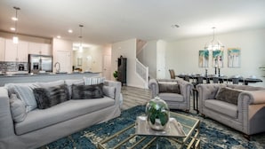 A spacious living room with two grey sofas, a coffee table with a globe, and a dining area with a chandelier. - The Ultimate Guide to Renting Your 5 Star Villa on Champions Gate Resort, Orlando Mansion 1817 (Davenport)