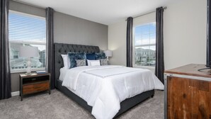 A modern hotel room with a large bed, grey curtains, a wooden nightstand, and a view of buildings through the window. - At Last You can Rent the Perfect Luxury Mansion on Champions Gate Resort, Minutes From Disney World, Orlando Mansion 3117 (Davenport)
