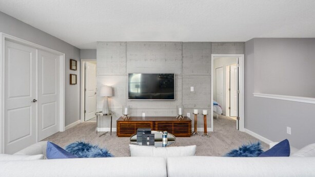 A living room with a flat-screen TV mounted on the wall, a wooden entertainment unit, a white sofa with blue throw pillows, and a ceiling light fixture. - At Last You can Rent the Perfect Luxury Mansion on Champions Gate Resort, Minutes From Disney World, Orlando Mansion 3117 (Davenport)