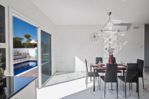 A dining area with a pool view, a modern chandelier, and a dining table set for four. - Cyprus Villa Minutes From the Beach, Protaras Villa 1195 (Paralimni)