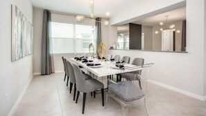 A modern dining area with a long table, grey chairs, and a chandelier. - Beautiful Mansion With Private Pool, Close to Disney, Orlando Mansion 3113 (Kissimmee)