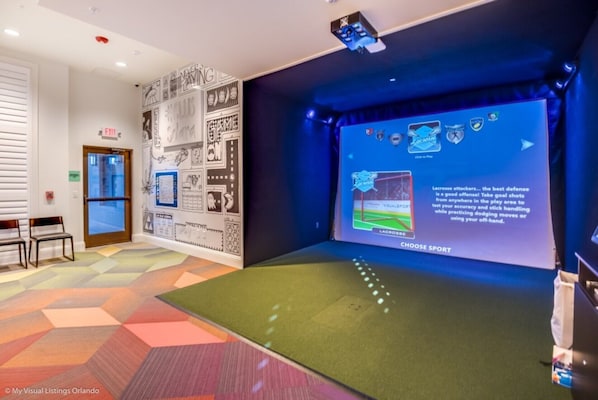 A room with a projection screen displaying a sports game, a green exercise mat, and a wall with various sports-related graphics.