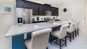 A kitchen with dark cabinets, a stainless steel refrigerator, a microwave, and a large island with bar stools. - Exclusive 5 Star Villa With Private Pool on Solara Resort, Orlando Villa 4843 (Kissimmee)