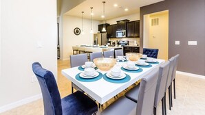 A modern dining area with a white table set for six, surrounded by grey chairs. - Modern Oasis With 7 Bedrooms & Garden 5524 (Kissimmee)