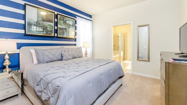 A bedroom with a bed, bedside tables, a TV, and a bathroom visible through an open door. - Modern Oasis With 7 Bedrooms & Garden 5524 (Kissimmee)