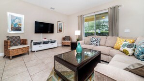 A living room with a flat-screen TV, wicker furniture, a sofa with patterned cushions, and a glass coffee table. - Private Oasis With 5 Bedrooms and Pool 5027 (Davenport)