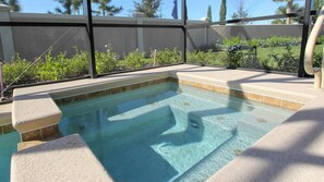 Un jacuzzi rectangulaire à l’eau claire, entouré d’une terrasse carrelée de couleur beige et d’un écran noir assurant l’intimité.