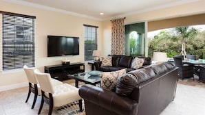 A living room with a leather sofa, a TV mounted on the wall, and a dining area with outdoor seating. - Beautiful Villa With First Class Amenities on Reunion Resort and Spa, Orlando Villa 4582 (Kissimmee)