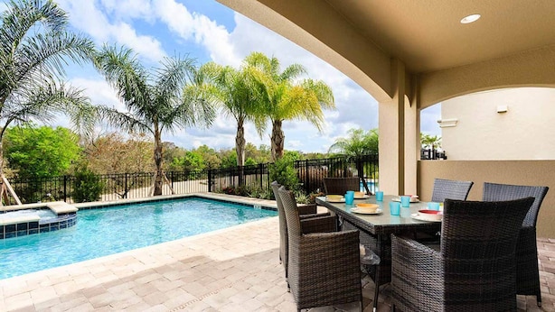 A poolside area with a table and chairs, surrounded by palm trees and a clear sky. - Beautiful Villa With First Class Amenities on Reunion Resort and Spa, Orlando Villa 4582 (Kissimmee)