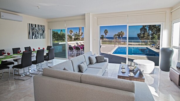 Ein modernes Wohnzimmer mit einer großen Couch, Essbereich mit Stühlen und Blick auf einen Pool.