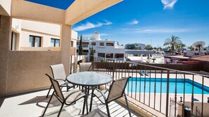 Ein Balkon mit Glastisch und Stühlen, mit Blick auf einen Swimmingpool und Gebäude.