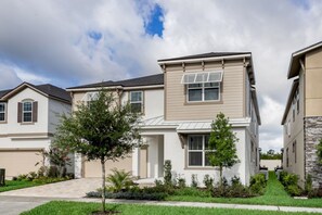 A residential building with a two-story design, featuring a front entrance, a garage, and a landscaped yard with small trees and shrubs.