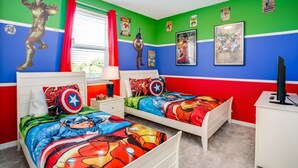 Un dormitorio con dos camas, paredes verdes y azules, ropa de cama con temática de superhéroes y varios pósteres.