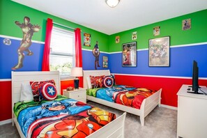Ein Schlafzimmer mit zwei Betten, grünen und roten Wänden sowie Bettwäsche und Postern zum Thema Superhelden.