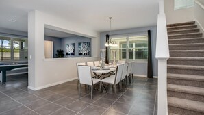 Un comedor amplio con una lámpara moderna, mesa de billar y una escalera que sube a un nivel superior.