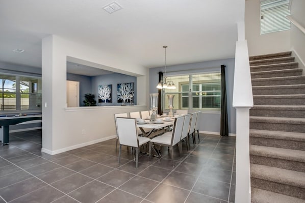 A spacious dining area with a modern chandelier, a pool table, and a staircase leading to upper levels.