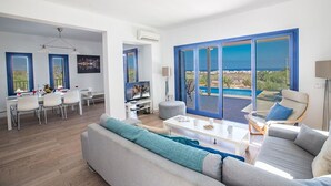 Un salon moderne doté d’un grand canapé, d’un coin repas avec des chaises et offrant une vue sur la mer grâce à de grandes fenêtres.