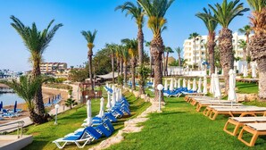 Un complexe hôtelier doté de rangées de chaises longues et de parasols, de palmiers et d’un espace piscine.
