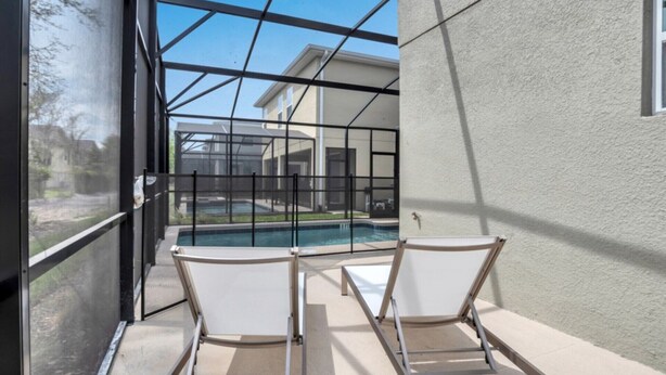 An outdoor pool area with two lounge chairs, a glass enclosure, and a view of a house in the background. - Luxury 5 Star Villa on Storey Lake Resort,minutes From Disney World, Orlando Villa 3654 (Kissimmee)