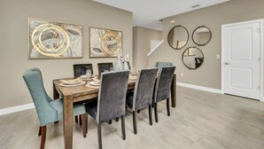 A dining area with a wooden table, six chairs, and three abstract paintings on the wall. - Luxury 5 Star Villa on Storey Lake Resort,minutes From Disney World, Orlando Villa 3654 (Kissimmee)