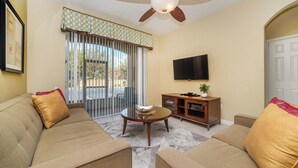 A living room with a sofa, a coffee table, a TV, and a sliding glass door. - Rent Your Own Exclusive Condo on Windsor Hills Resort, Orlando Condo 4783 (Kissimmee)