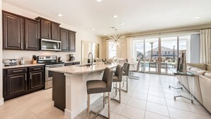 A modern kitchen with dark cabinets, a central island, and a dining area with bar stools. - Beautiful Villa With First Class Amenities on Encore Resort at Reunion, Orlando Villa 4708 (Kissimmee)