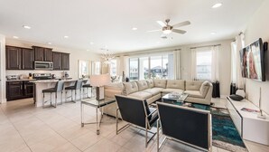 A modern living room with a sectional sofa, a glass coffee table, and a dining area with bar stools. - Beautiful Villa With First Class Amenities on Encore Resort at Reunion, Orlando Villa 4708 (Kissimmee)