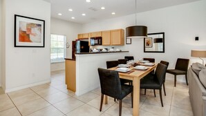 A modern kitchen with wooden cabinets, a central island, and a dining area with a table set for four. - Enjoy a Holiday of a Lifetime in This Luxury Home on Encantada Resort, Orlando Townhome 3662 (Kissimmee)