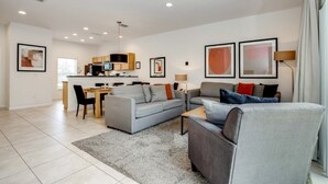 A modern living room with a grey sofa, a dining area with a table and chairs, and a kitchen in the background. - Enjoy a Holiday of a Lifetime in This Luxury Home on Encantada Resort, Orlando Townhome 3662 (Kissimmee)