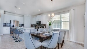 A modern kitchen with white cabinets, a central island, and a dining area with grey upholstered chairs and a wooden table. - Luxury Villa on Solara Resort With Private Pool, Orlando Villa 2020 (Kissimmee)