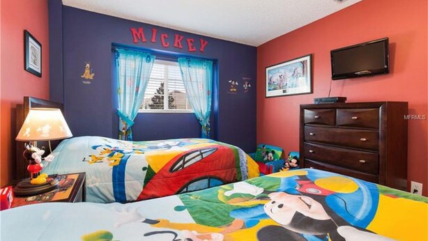 Een kinderkamer met een sprei met Mickey Mouse motief, een kapstok en een televisie aan de muur.