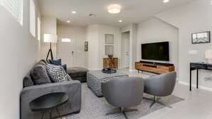 A modern living room with a grey sofa, a coffee table, and two armchairs. A flat-screen TV is mounted on the wall, and there is a wooden cabinet below it. - Elegant 5 Bed Villa Near Disney, 3472 (Kissimmee)