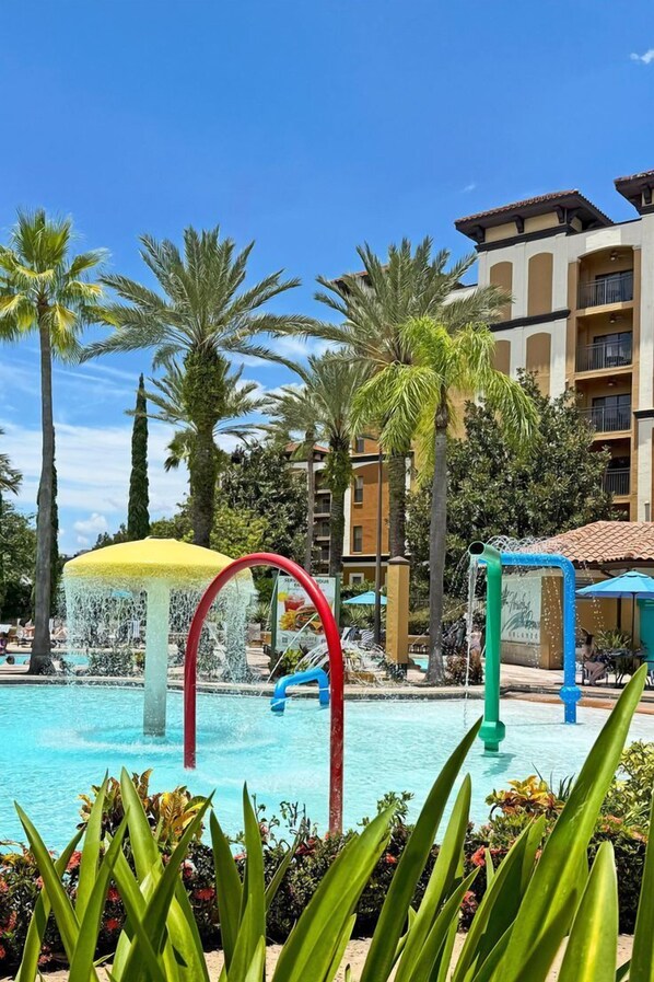 A swimming pool with water features and palm trees, surrounded by multi-story buildings. - Beautiful Villa With First Class Amenities on Reunion Resort and Spa, Orlando Villa 4577 (Kissimmee)