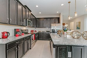A modern kitchen with dark cabinets, a granite countertop, stainless steel appliances, and pendant lighting. - Beautiful Villa With Private Pool, Close to Disney, Orlando Villa 3124 (Kissimmee)