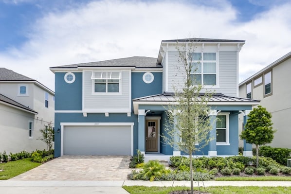 A two-story residential building with a garage, a front porch, and a small garden area.