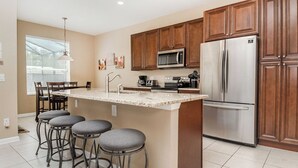 Una cocina con una isla central, taburetes de bar, un refrigerador y armarios de madera.