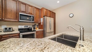 Una cocina con armarios de madera, un refrigerador de acero inoxidable, un microondas, una estufa y una encimera de granito.
