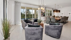Ein modernes Wohnzimmer mit grauen Sofas, einem Essbereich mit Esstisch für sechs Personen und einem großen Fenster mit Blick ins Freie.