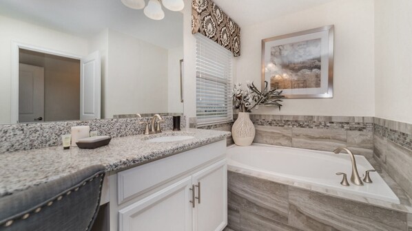 A modern bathroom with a granite countertop, a large mirror, a bathtub, and a decorative wall piece. - 5 Star Villa With Private Pool, Orlando Villa 4899 (Kissimmee)
