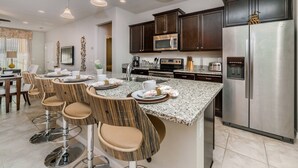 A modern kitchen with dark wood cabinets, stainless steel appliances, and a granite countertop. - Exclusive Villa With Large Private Pool on Windsor at Westside Resort, Orlando Villa 4974 (Kissimmee)