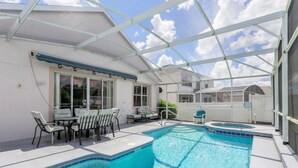 A covered outdoor swimming pool with lounge chairs and a table, surrounded by a glass enclosure. - Imagine Your Family Renting This Luxury Villa on Highlands Reserve, Orlando Villa 3607 (Davenport)