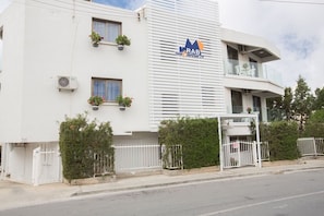 Un bâtiment moderne avec une enseigne indiquant « RAB Tour & Travel Enterprises Ltd. ». Il est doté d’un balcon avec des balustrades blanches, de plantes en pot sur les rebords de fenêtres et d’une entrée fermée par un portail.